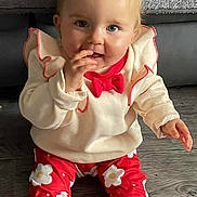 Brianna joined the competition — help win amazing prizes! baby, child, sitting, floor, red_pants, flower_pattern, cream_sweater, red_bow, sock, wooden_floor, indoor, person, cute, smiling, face, fingers, curious, cozy, blanket, couch