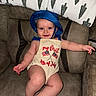 baby, child, smile, blue_hat, romper, couch, sitting, cute, happy, indoor, infant, clothing, face, person, skin, legs, arms, text_on_clothing, celebration, holiday