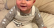 Sutton is registered to the contest to win money with this photo: baby, bed, blanket, blue_eyes, child, cozy, cute, fabric, face, hair, happy, indoors, infant, overalls, pajamas, person, sitting, sleepwear, smiling, socks