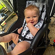 Sutton is registered to the contest to win money with this photo: baby, child, stroller, outdoor, smile, blue_eyes, onesie, mickey_mouse, cute, happy, playful, seatbelt, hand, legs, sunlight, black_stroller, mesh_canopy, concrete_ground, infant, person