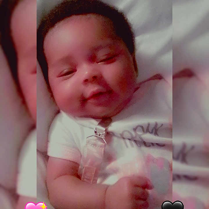 Ayannah is registered to the contest to win money with this photo: baby, baby_face, black_heart, child, close_up, cute, emoji, face, hand, happy, indoors, infant, lying_down, pacifier_clip, pink_heart, portrait, skin, smiling, soft_surface, white_clothing
