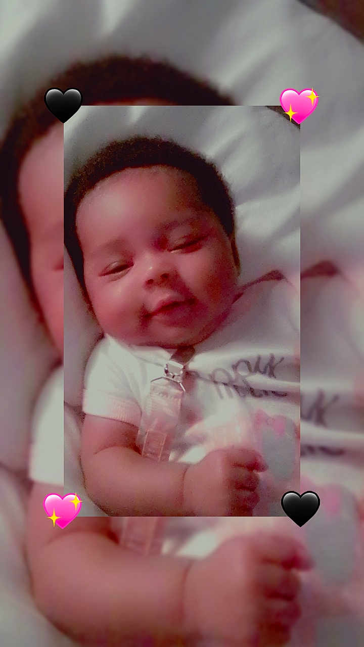Ayannah is registered to the contest to win money with this photo: baby, child, smiling, infant, white_clothing, pacifier_clip, close_up, indoors, cute, happy, face, skin, hand, lying_down, soft_surface, black_heart, pink_heart, emoji, portrait, baby_face
