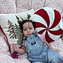 baby, child, infant, overalls, striped_clothing, pink_shirt, fluffy_chair, pillows, christmas_pillow, peppermint_pillow, embroidered_pillow, indoor, cute, relaxed, portrait, person, soft_texture, holiday_theme, seated, young