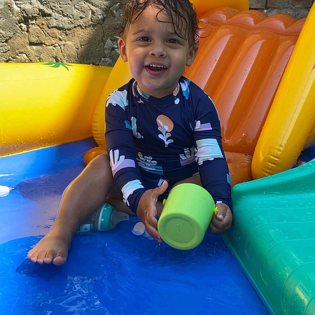 Zackaria participe au concours pour gagner de l'argent avec cette photo : blue, child, colorful, cup, green, happy, inflatable, orange, outdoor, play, pool, sitting, smiling, stone_wall, summer, toddler, toy, water, wet_hair, yellow