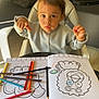 art_supplies, child, clothing, colored_pencils, coloring_book, cushions, drawing, expression, eyes, face, furniture, hair, high_chair, indoor, person, play, sitting, table, toddler, wooden_floor