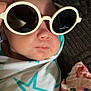 baby, sunglasses, blanket, star_pattern, face, person, infant, wrapped, head, expressionless, indoor, clothing, quilt, fabric, closeup, skin, hand, nose, mouth, eyewear