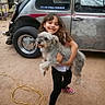 child, dog, smiling, outdoor, car, vintage_car, veteran_sticker, dirt_ground, casual_clothing, red_shoes, polka_dot, pet, happy, hair, holding, vehicle, wheel, window, person, animal