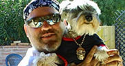 Abbeyroad is registered to the contest to win money with this photo: bandana, beard, black_clothing, casual, dog, fence, greenery, happy, holding, man, necklace, outdoor, pet, portrait, relaxed, skull, small_dog, sunglasses, sunlight, yard