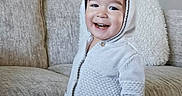 Theodore joined the competition — help win amazing prizes! toddler, child, smile, hoodie, white_clothing, couch, beige, snack, happy, indoor, cozy, plush_pillow, knitwear, cute, person, young_child, casual_wear, home, portrait, standing