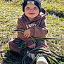 Maélïo a rejoint le concours — aidez-le/la à gagner de superbes lots ! toddler, child, grass, outdoor, sunlight, beanie, black_hat, hoodie, brown_clothing, smiling, happy, playful, strap, shoes, casual, nature, daylight, sitting, cute, young_child
