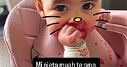 Penelope joined the competition — help win amazing prizes! baby, bib, child, dark_hair, eyes, face, floral_clothing, food, food_splatter, hand, hello_kitty_filter, high_chair, indoors, infant, kitchen, pink, portrait, sitting, smiling, text_overlay