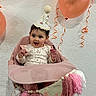 Penelope is registered to the contest to win money with this photo: baby, child, birthday, birthday_hat, balloons, pink, high_chair, sitting, smiling, open_mouth, indoors, party, celebration, decorations, tassels, ribbons, festive, floral_outfit, portrait, wooden_floor