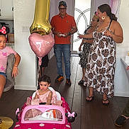 Penelope is registered to the contest to win money with this photo: child, toddler, birthday, party, toy_car, pink, balloon, number_one, family, adults, indoor, celebration, streamers, dress, sitting, smiling, home, wood_floor, decorations, portrait
