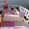Penelope is registered to the contest to win money with this photo: children, toddlers, baby, ball_pit, slide, playpen, outdoor, pastel, pink, white, toy_fence, playground, photographer, camera, flowers, minnie_mouse, dress, cap, sitting, playtime