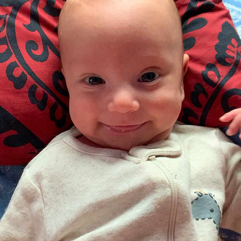Xavier is registered to the contest to win money with this photo: baby, clothing, coat, couch, cushion, face, furniture, happy, head, homedecor, jacket, laughing, newborn, pants, person, photography, portrait, quilt, smile, t_shirt