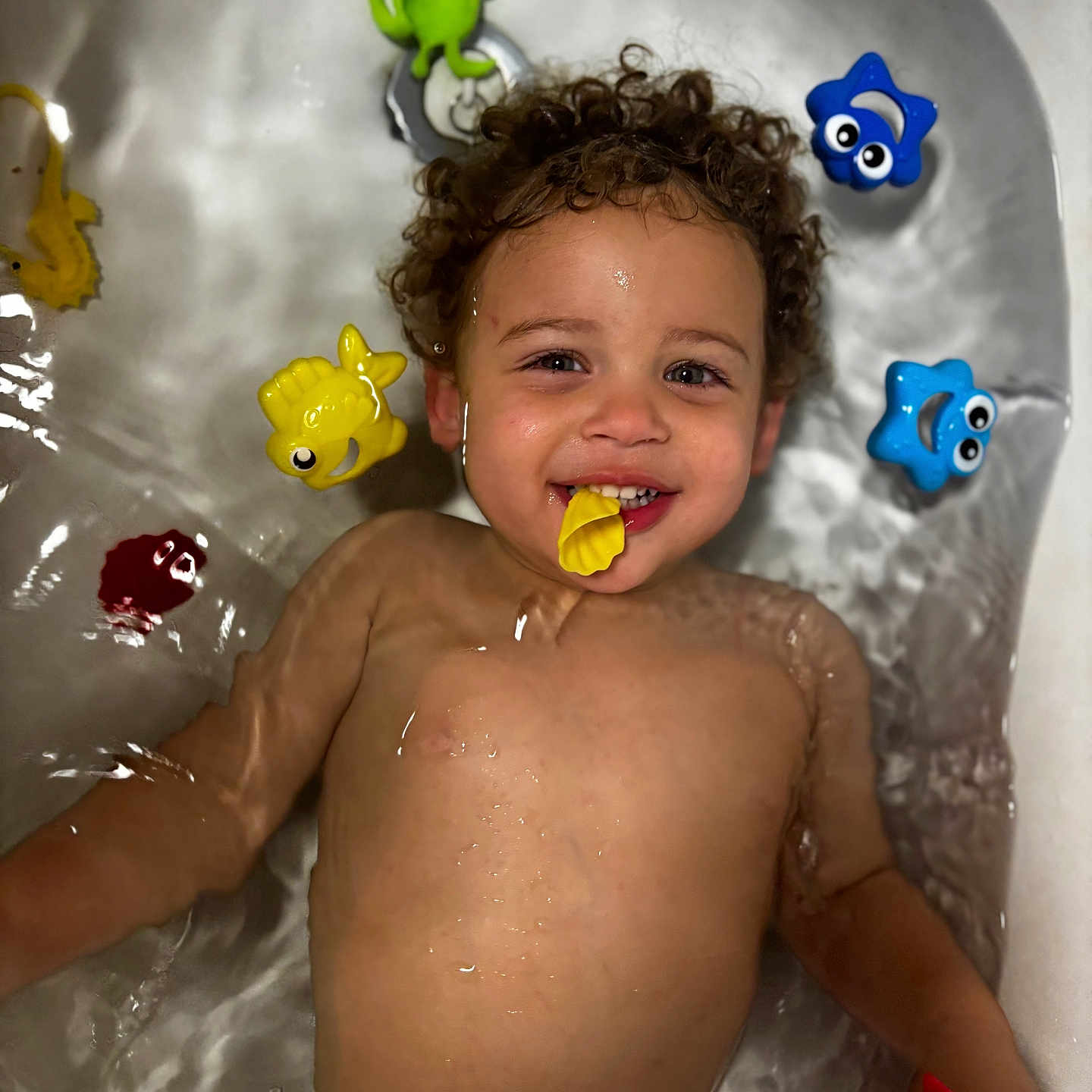 Jace is registered to the contest to win money with this photo: animal, baby, babylaughing, bathing, bathtub, bubble, dinosaur, earbuds, electronics, face, happy, head, indoors, person, photography, portrait, reptile, smile, toy, tub
