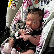 Billie is registered to the contest to win money with this photo: baby, infant, pacifier, car_seat, floral_pattern, bracelet, pink_socks, child, newborn, seatbelt, cute, portrait, indoors, soft_toys, baby_accessory, hand, face, head, person, sitting