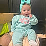 baby, blanket, bow, cardboard_box, child, cute, dark_wood, furniture, hand, headband, indoor, infant, mint_green, pants, person, portrait, seated, smiling, socks, sweatshirt