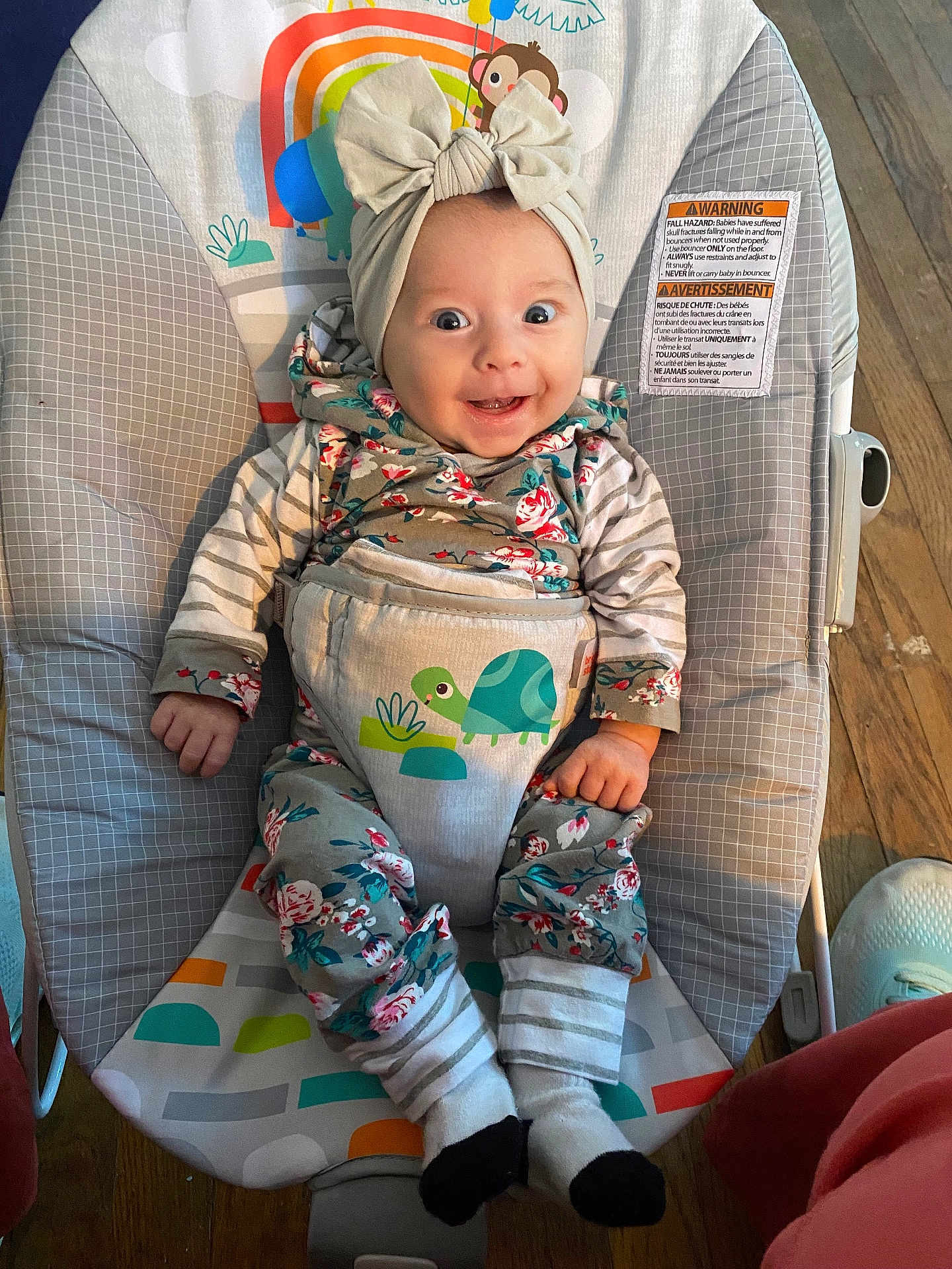 Paisley joined the competition — help win amazing prizes! baby, infant, smiling, headband, bow, bouncer, turtle, clothing, patterned_clothes, socks, wooden_floor, happy, cute, child, indoor, person, seat, baby_seat, floor, colorful
