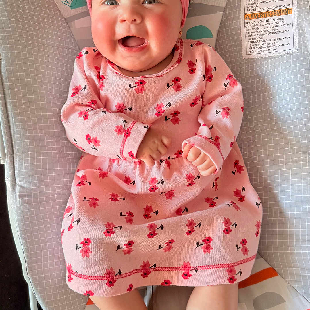 Ailany is registered to the contest to win money with this photo: baby, infant, smiling, pink_dress, headband, baby_seat, colorful, happy, cute, child, floral_pattern, indoors, cheerful, monkey_design, sun_design, clothing, feet, portrait, sitting, young_child
