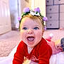 baby, child, smiling, laughing, flower_crown, red_clothing, blue_eyes, blanket, indoor, carpet, happy, cute, toddler, portrait, headwear, person, infant, cheerful, young_child, home