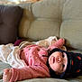 baby, infant, child, pink_sweater, knitted_hat, blanket, couch, indoor, portrait, cute, cozy, wide_eyes, rosy_cheeks, soft_lighting, relaxed, clothing, person, face, headwear, laying_down