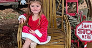 Adalyn joined the competition — help win amazing prizes! child, girl, red_dress, wooden_chair, holiday_decorations, jingle_bells, red_ladder, sign, autumn_leaves, outdoor, smiling, festive, christmas, rustic, portrait, cute, seasonal, person, sneakers, wood
