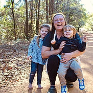 Johnny joined the competition — help win amazing prizes! woman, child, toddler, forest, dirt_path, trees, sunlight, happy, smiling, barefoot, casual_clothing, outdoor, nature, family, leaves, walking_path, blue_shoes, long_hair, crouching, daylight