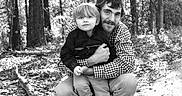 Johnny is registered to the contest to win money with this photo: child, man, outdoor, forest, hugging, black_and_white, nature, trees, leaves, portrait, family, casual_clothing, smile, person, candid, toddler, father_and_son, emotion, daylight, ground