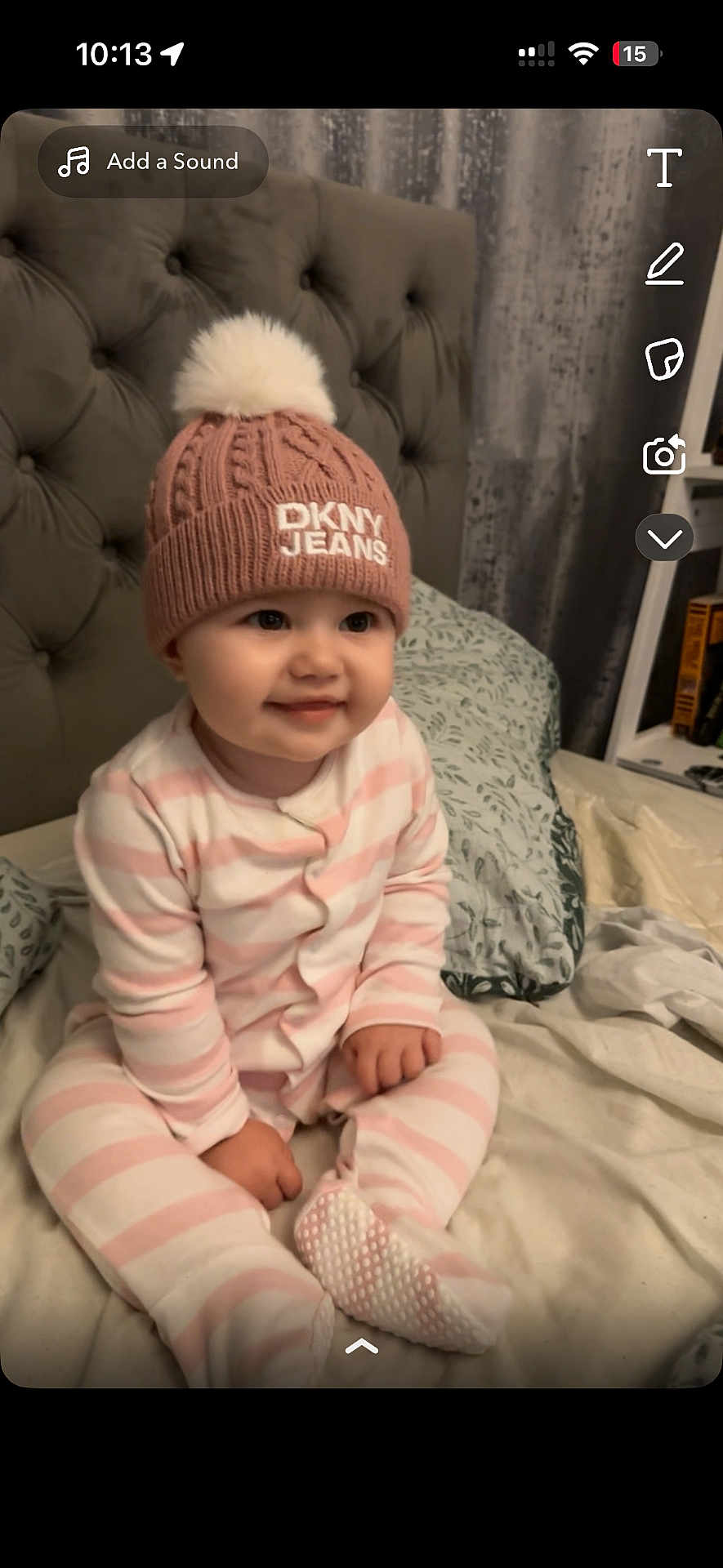 Vaiva is registered to the contest to win money with this photo: baby, child, infant, hat, knit_hat, pom_pom, pink, striped_clothing, onesie, bed, pillow, headboard, smiling, indoors, cozy, cute, person, face, sitting, sleepwear