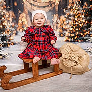 Vaiva is registered to the contest to win money with this photo: baby, child, sled, christmas, holiday, festive, plaid_dress, hat, smile, winter, snow, tree, lights, burlap_sack, wood, indoor, portrait, cute, happy, seasonal