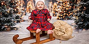 Vaiva is registered to the contest to win money with this photo: baby, burlap_sack, child, christmas, cute, festive, happy, hat, holiday, indoor, lights, plaid_dress, portrait, seasonal, sled, smile, snow, tree, winter, wood