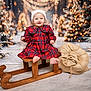 baby, child, sled, christmas, holiday, festive, plaid_dress, hat, smile, winter, snow, tree, lights, burlap_sack, wood, indoor, portrait, cute, happy, seasonal