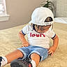 Lucas Valentino is registered to the contest to win money with this photo: child, toddler, sitting, bedroom, bed, backwards_cap, white_shirt, denim_shorts, sneakers, socks, indoor, portrait, looking_down, casual_clothing, fashion, long_hair, carpet, plant, window, furniture