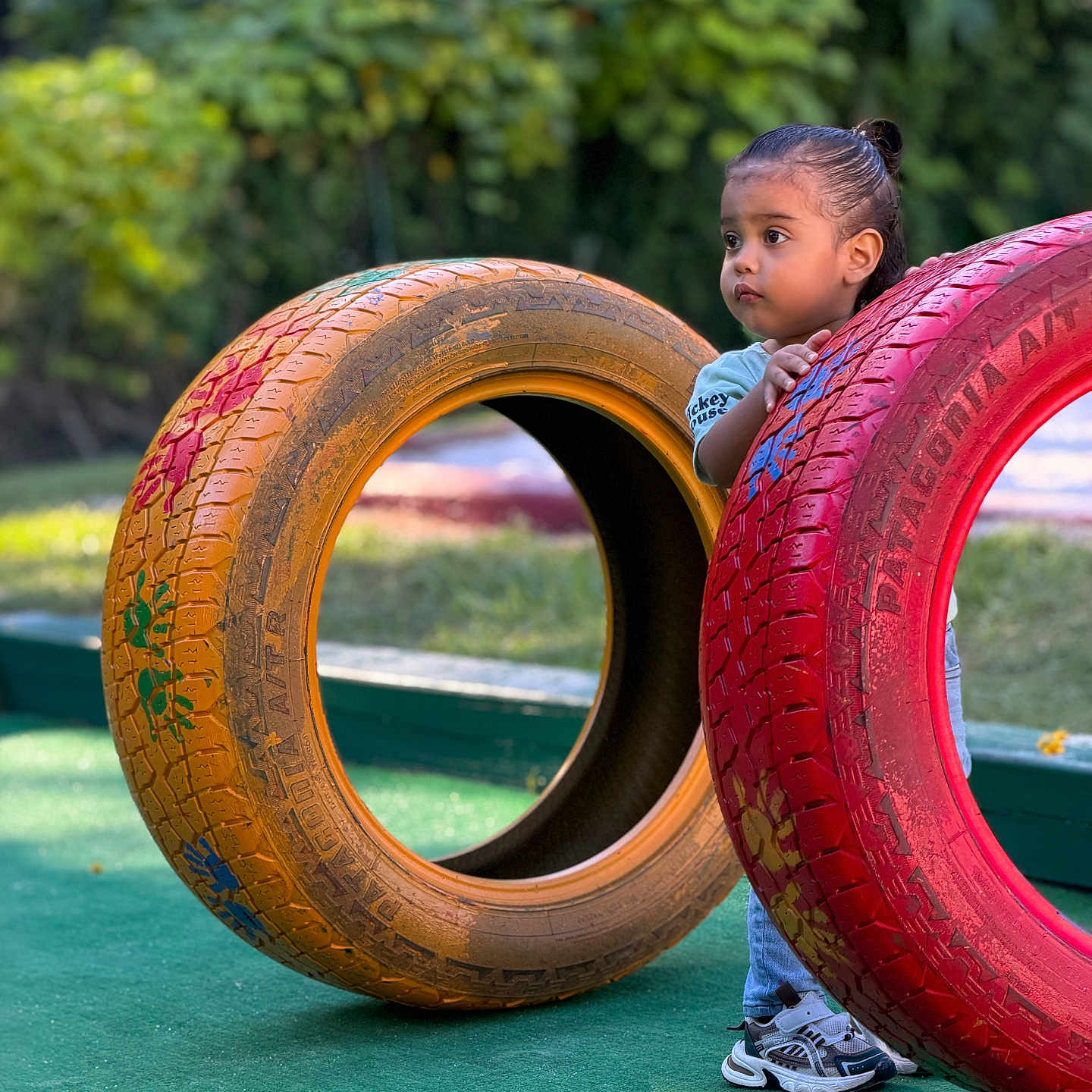Lucas Valentino joined the competition — help win amazing prizes! child, toddler, playground, tires, colorful, outdoor, garden, portrait, peeking, curious, standing, sneakers, blue_shirt, red_tire, yellow_tire, green_ground, trees, sunlight, play, photography