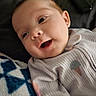 baby, infant, child, face, portrait, smiling, happy, open_mouth, lying_down, indoor, blanket, soft, clothing, onesie, ribbed_fabric, earring, close_up, warm_lighting, couch, adorable