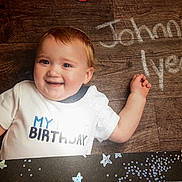 John joined the competition — help win amazing prizes! baby, child, birthday, smiling, portrait, lying_down, wooden_background, white_shirt, birthday_shirt, infant, happy, face, eyes, arms, outdoor_style, celebration, rustic, photography, closeup, family