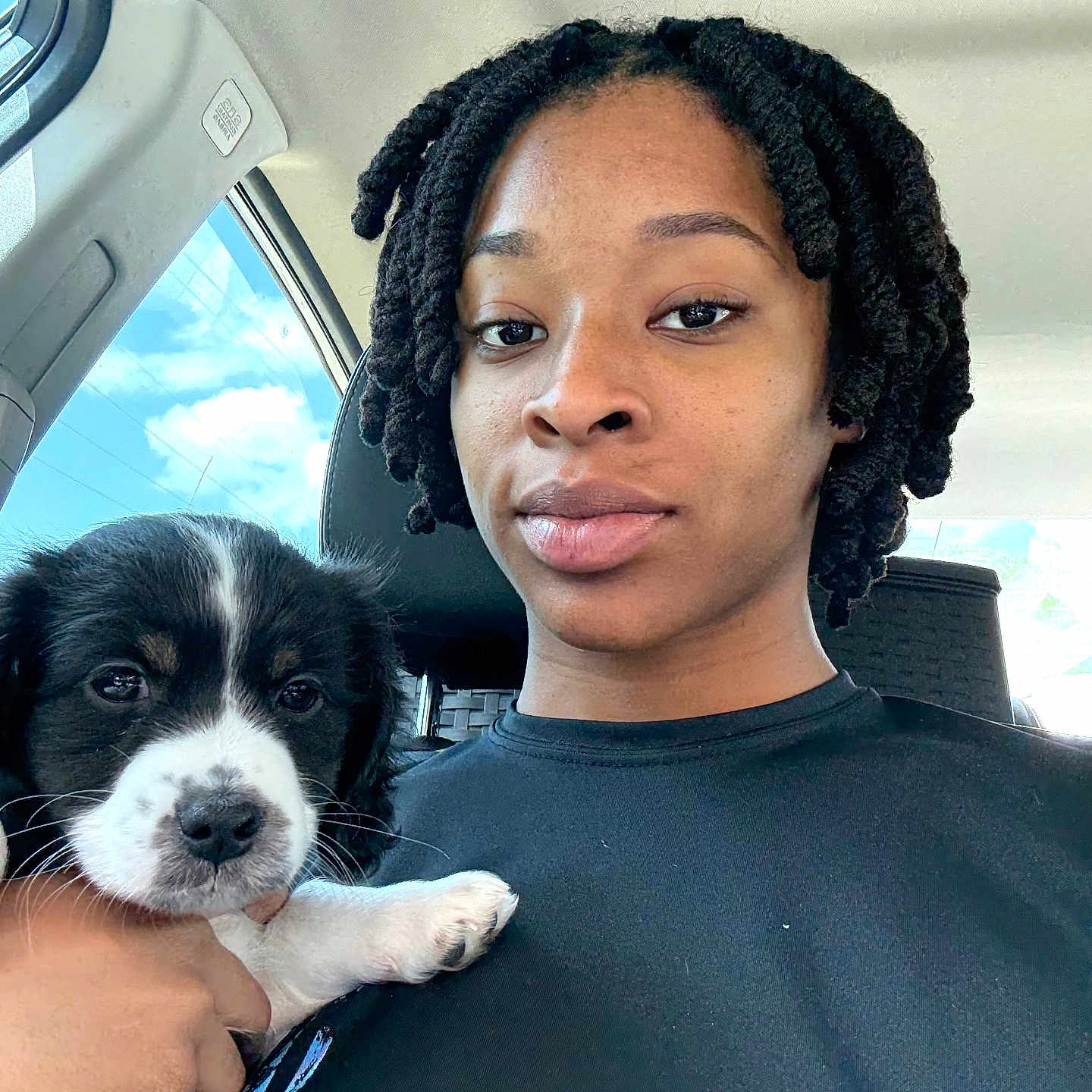 Oreo joined the competition — help win amazing prizes! black_hair, calm, car, casual_clothing, clouds, cute, daylight, dog, face, hand, indoor, person, portrait, puppy, seat, selfie, sky, twist_hairstyle, white_puppy_paw, window