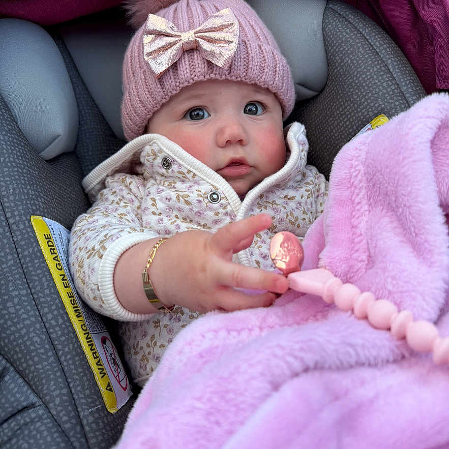 Sahily is registered to the contest to win money with this photo: baby, child, car_seat, hat, knit_hat, pom_pom, bow, blanket, pink, toy, clothing, cozy, cute, portrait, infant, warm, bundle, expression, person, indoor
