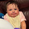 Sahily is registered to the contest to win money with this photo: baby, pout, bib, pink_shirt, balloons, leather_couch, chubby_cheeks, curly_hair, indoor, portrait, child, cute, expression, sitting, closeup, face, person, infant, young_child, home