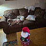 dog, couch, living_room, pillow, decor, wooden_table, carpet, painting, lamp, wall, floor, holiday_decor, santa, stuffed_toy, pet, relaxing, indoor, furniture, cozy, three_dogs