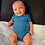 Zorie is registered to the contest to win money with this photo: baby, smile, blue_onesie, infant, bed, pillow, blanket, skin, happy, cute, child, portrait, sitting, indoors, person, young_child, chubby_arms, legs, head, expression