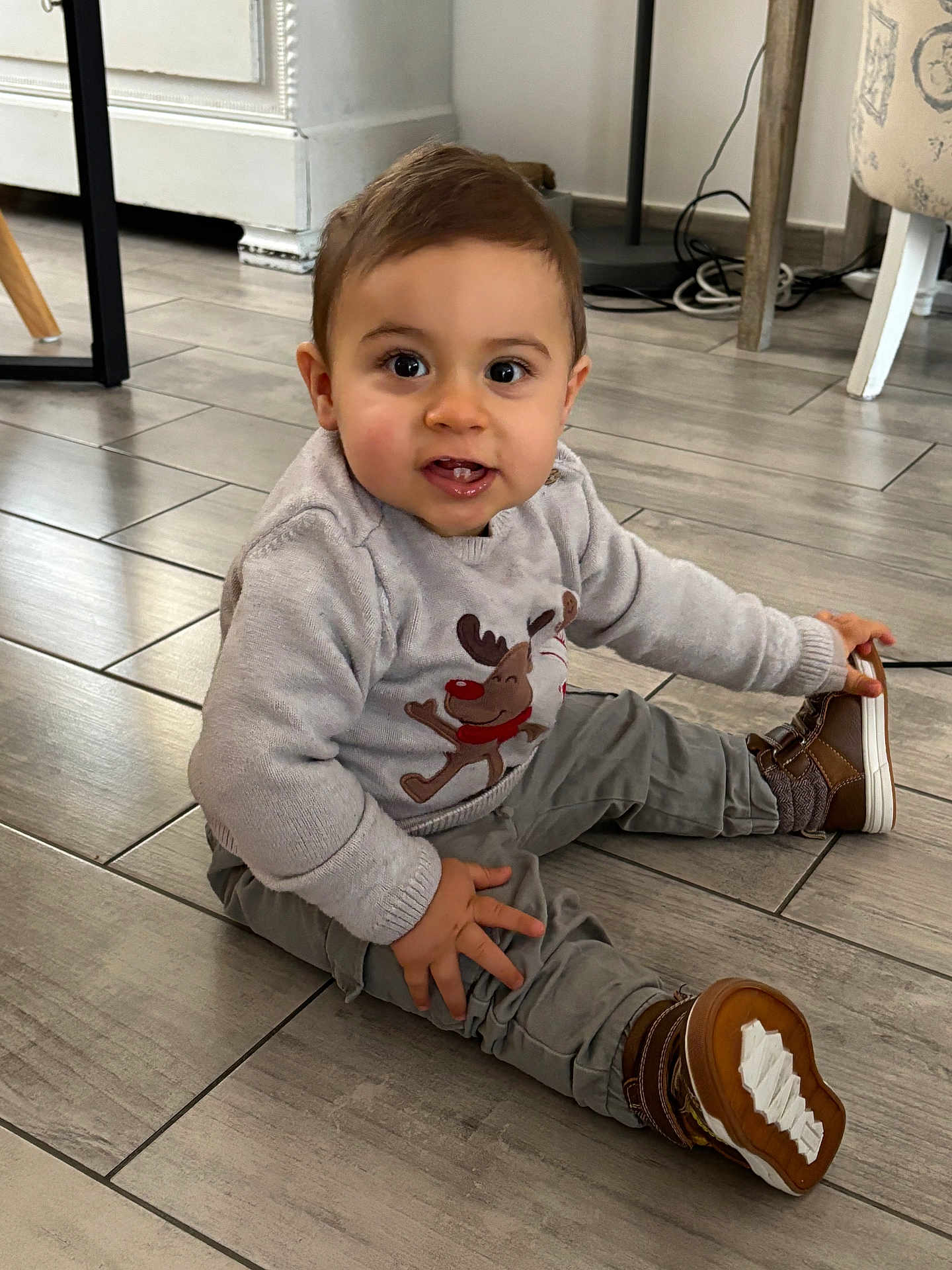 Robin a rejoint le concours — aidez-le/la à gagner de superbes lots ! toddler, child, floor, tile, sweater, reindeer, brown_shoes, pants, indoor, curious_expression, smile, hand, seated, person, young_child, cozy_clothing, flooring, candid, cute, playful
