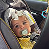Amelia is registered to the contest to win money with this photo: baby, infant, child, car_seat, pacifier, bow, striped_clothing, yellow_clothing, car, vehicle, travel, backseat, safety_harness, toy, window, palm_trees, outdoor, portrait, looking_at_camera, daylight