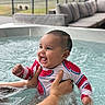 baby, child, infant, smiling, happy, water, hot_tub, swimming, swimwear, watermelon_pattern, outdoor, patio, sofa, adult_hand, supported, splashing, portrait, close_up, family, recreation