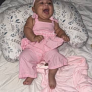 Amelia is registered to the contest to win money with this photo: baby, child, infant, smiling, laughing, headband, pink_clothing, striped_outfit, dress, pajamas, sitting, bed, bedding, blanket, pillow, nursing_pillow, bedroom, indoors, portrait, happy