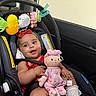 Amelia is registered to the contest to win money with this photo: baby, infant, child, car_seat, car, travel, portrait, smiling, happy, plush_toy, doll, baby_toys, red_clothing, headband, socks, safety_harness, indoors, vehicle, close_up, family