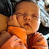 Devyn is registered to the contest to win money with this photo: baby, caregiver, child, close_up, closed_eyes, cozy, cute, face, hand, indoors, infant, orange_clothing, peaceful, person, portrait, resting, sitting, sleeping, soft_focus, warm_lighting