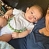 baby, infant, child, person, adult, couch, leather_couch, blanket, clothing, pacifier, relaxing, indoor, portrait, holding, blue_shirt, white_onesie, skin, face, looking, seated
