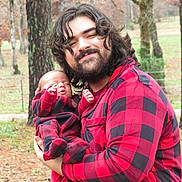 Hollie is registered to the contest to win money with this photo: man, baby, infant, outdoor, forest, trees, autumn, matching_outfits, plaid, red_and_black, smiling, beard, long_hair, holding, nature, peaceful, portrait, parent_and_child, fall_leaves, clothing